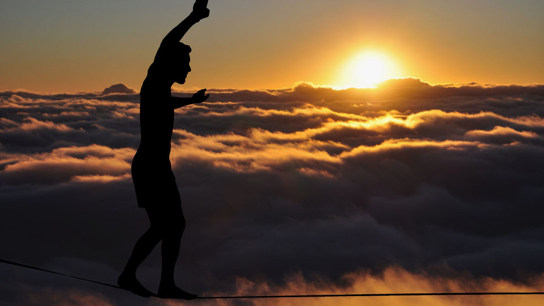 Man balancing on tight rope at sunset with clouds in the background.