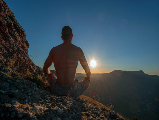 A man sits in a peaceful meditation pose on top of a mountain, surrounded by nature.