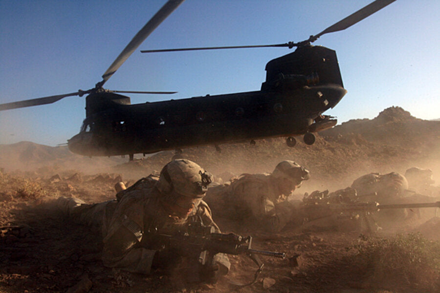Helicopter landing in desert with two soldiers on the ground in military gear