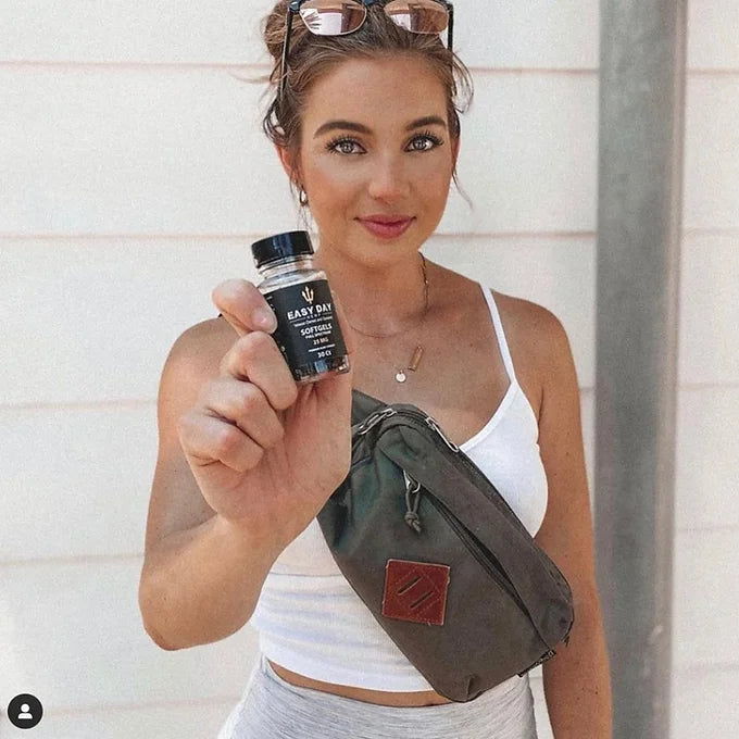 A fit and attractive woman confidently holding a bottle of 25mg CBD Softgels, emphasizing their role in promoting a healthy lifestyle and restorative sleep.