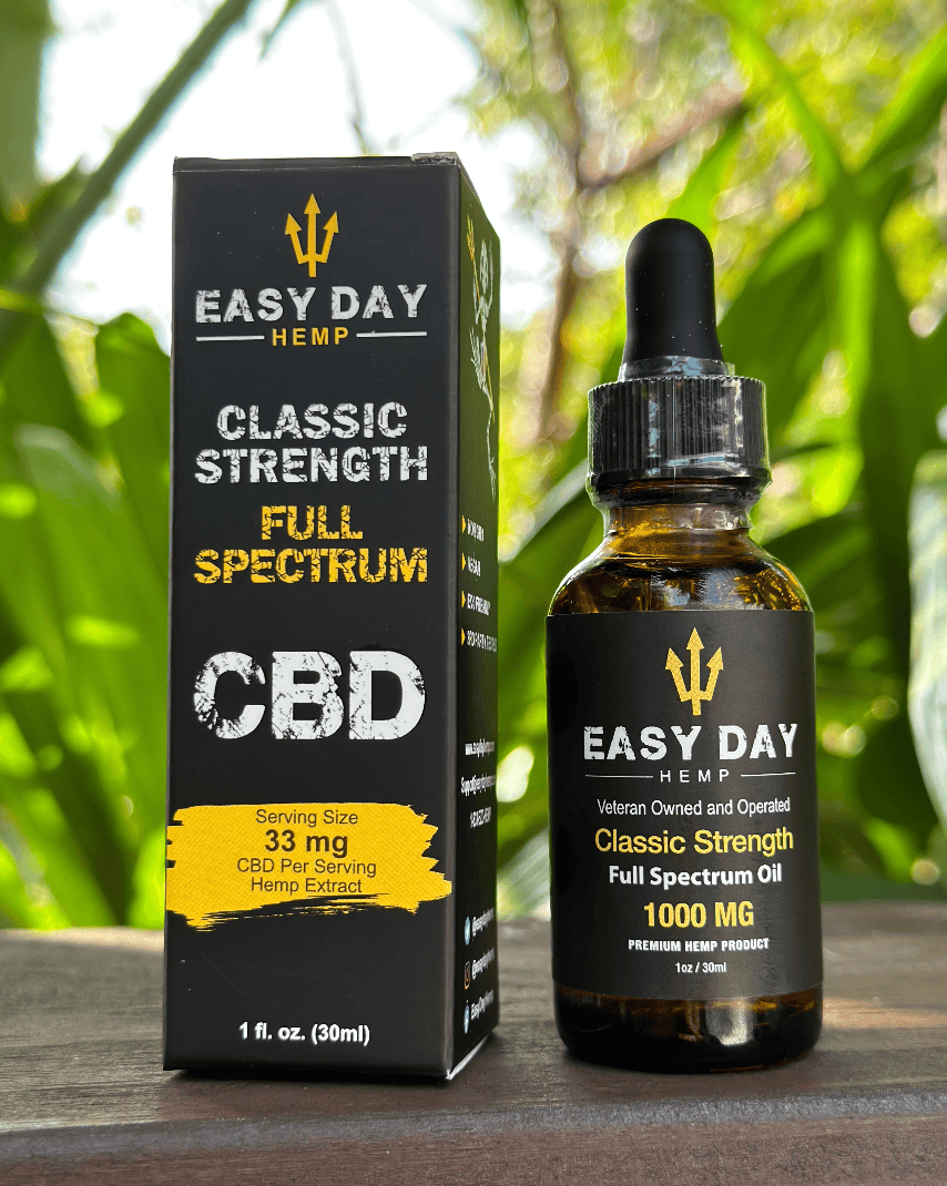 A brown bottle of Easy Day Hemp Classic strength 1000mg full spectrum CBD oil with a black label listing the ingredients and dosage instructions, sitting next to a box with a gold Easy Day logo and a jungle background. This CBD oil is great for promoting overall wellness and may have potential benefits for anxiety, pain relief, and sleep.